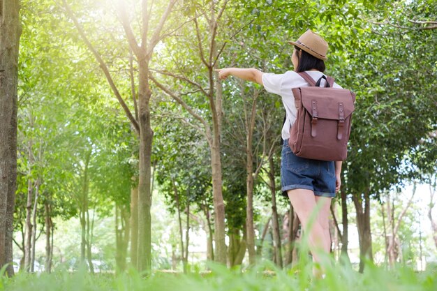 Asian woman pointing in grass fields forest tree outdoors.