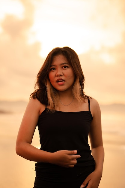 An asian woman poses with a dirty and angry expression when wearing a black dress on the beach