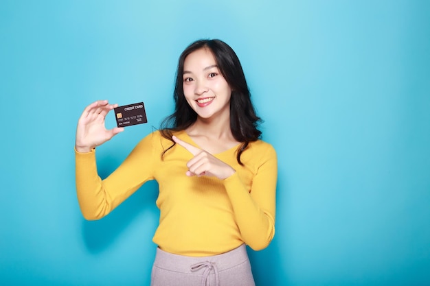 아시아 여성이 신용카드를 들고 포즈를 취하고 있다. 밝은 파란색 배경의 아름다운 젊은 여성의 초상화.