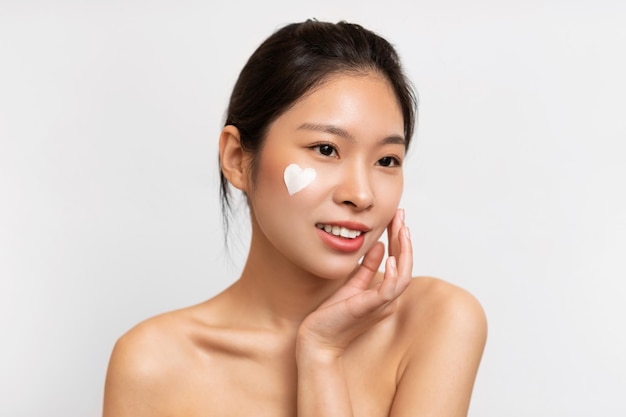 Photo asian woman posing with heart shaped cream on cheek