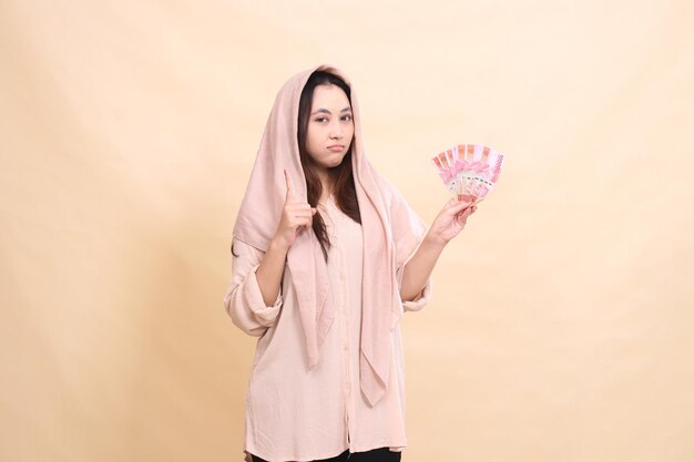 Photo asian woman pouting at the camera with her hand pointing up and carrying rupiah money for the compet