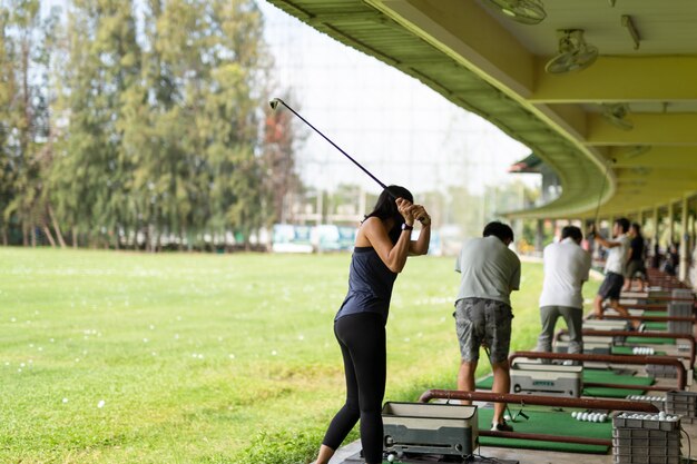 Donna asiatica che si esercita nella sua oscillazione di golf alla gamma di azionamento di golf.