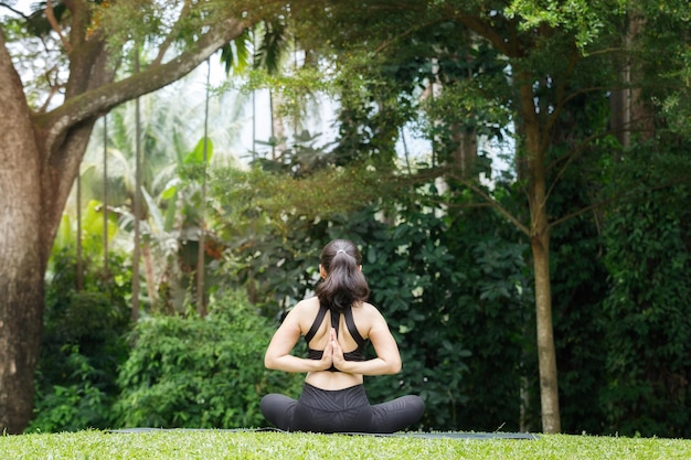 Donna asiatica che pratica yoga nella posa del loto di preghiera inversa, schiena e spalle che si allungano nel parco all'aperto.