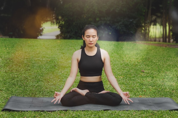 Donna asiatica che pratica yoga in root bond, posa di mula bandha sul tappeto nel parco all'aperto.