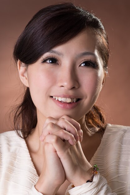 Asian woman praying, closeup portrait on studio brown background.