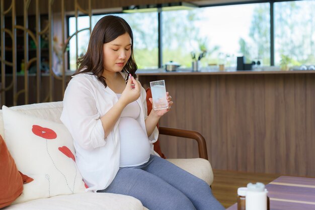 Asian woman pregnant mother holding medicine supplement drugs and glass