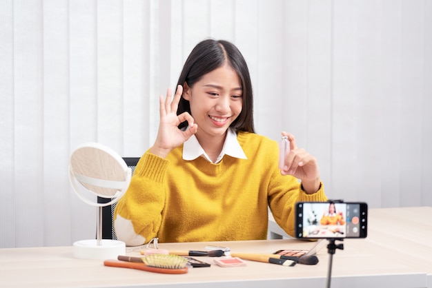 Asian woman present beauty cosmetic product and broadcast live video to social network by internet at home, beauty blogger concept.