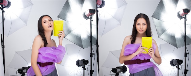 Asian woman in purple clothes, shows green package which has empty green area for advertising, in studio with umbrella light background copy space