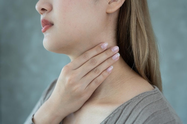 Asian woman put her hand on her neck due to a sore throat female tonsillitis causes a inflammation treated by taking water taking antibiotics consult a doctor virus corona virus Influenza flu