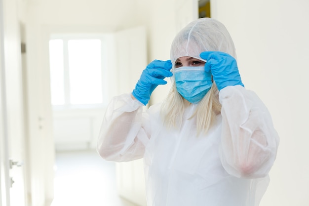 Asian woman puts on a protective mask and suit. Protected against flu, ebola, tuberculosis, virus. Personal protective equipment against biological hazard.