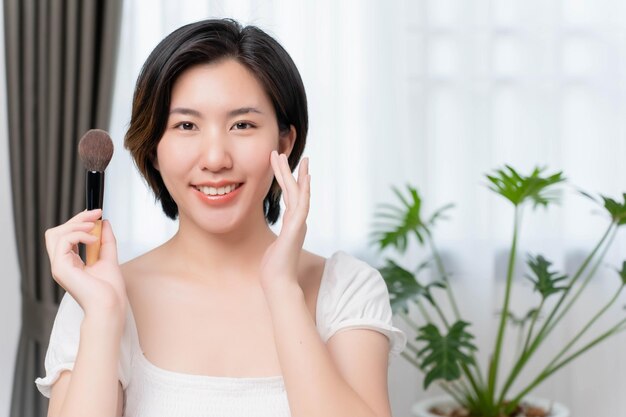 Asian woman putting makeup on in bedroom before going out