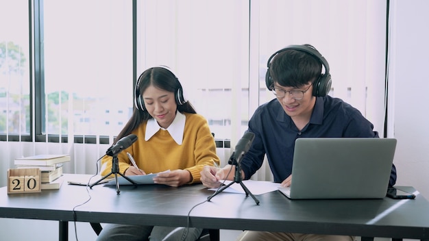 Asian woman radio hosts gesturing to microphone while interviewing a man guest in radio station during a show for radio live in the Studio.