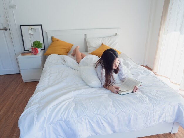 Asian woman reading book on bed in the morning