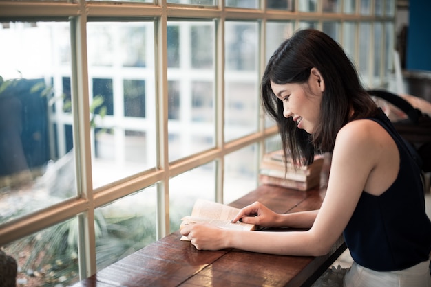 Donna asiatica che legge un libro al coffeeshop.