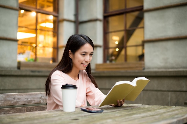 屋外カフェで本を読むアジア人女性