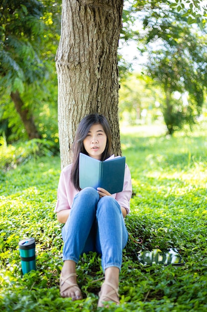 Азиатская женщина, читающая книгу и улыбаясь в парке