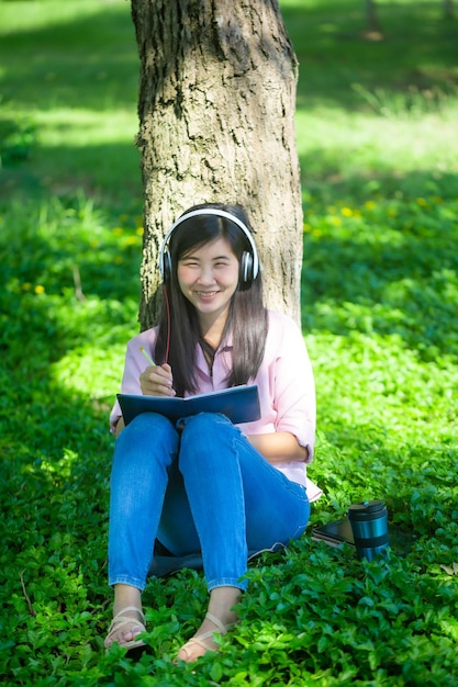 Азиатка читает книгу и улыбается в паркеУдовлетворенная азиатка читает книгу в парке