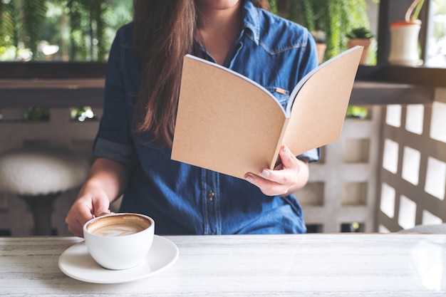 Asian woman reading a book while drinking coffee in modern cafe