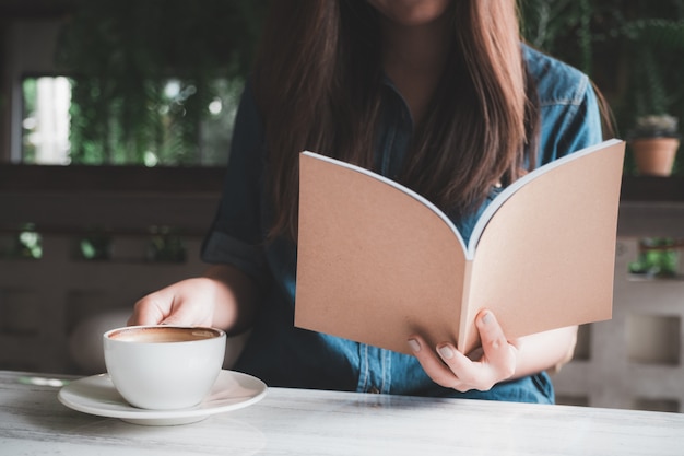 Asian woman reading a book while drinking coffee in modern cafe