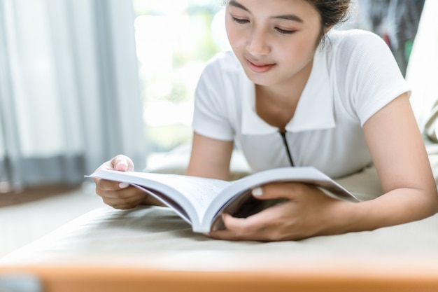 Asian woman reads an analog book on the sofa.