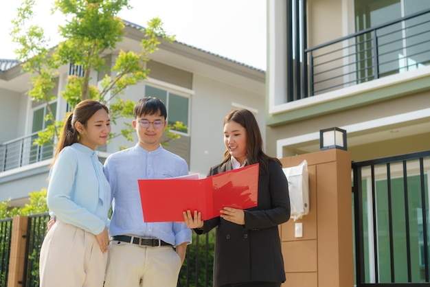 아시아 여성 부동산 중개업자가 젊은 아시아 커플 연인에게 파일에 있는 집 세부 정보를 보여주고 구매에 관심을 갖고 있습니다.