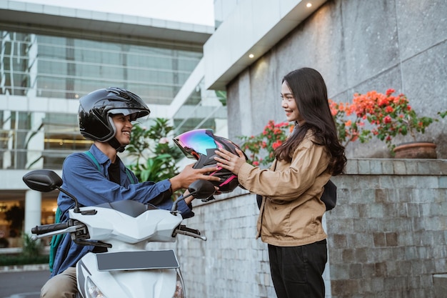 Asian woman receiving helmet from man riding motorbike on roadside