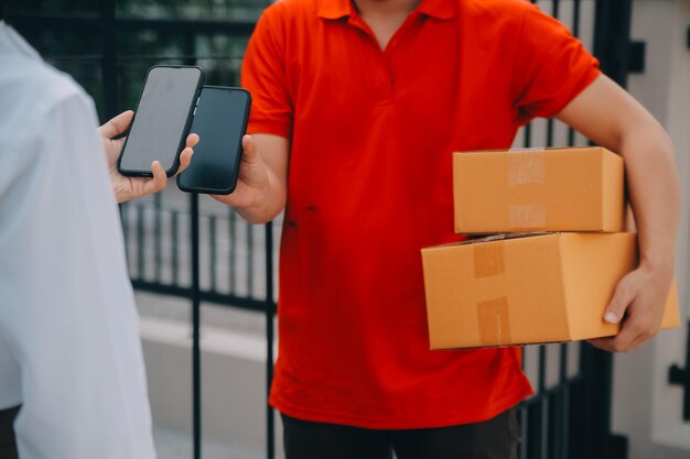 Photo asian woman receiving product from delivery man at home young owner woman order product from smartphone application woman with online business or sme concept