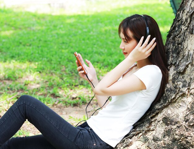 Asian woman relax by listening to music on smartphones happily in the park.