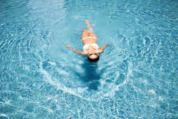 La donna asiatica si rilassa sulla piscina d'acqua in estate prende il sole felice in piscina e la suite bikini e gli occhiali da sole