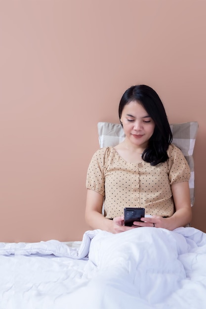 Donna asiatica che si rilassa a letto mentre si tiene il telefono cellulare