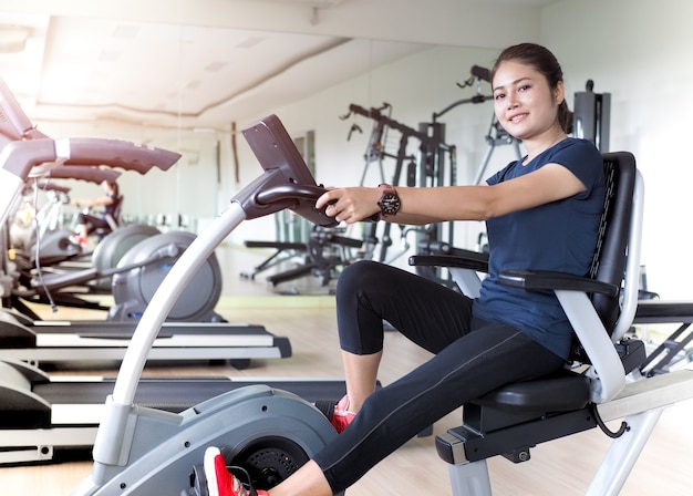 Asian woman riding stationary bike in gym.