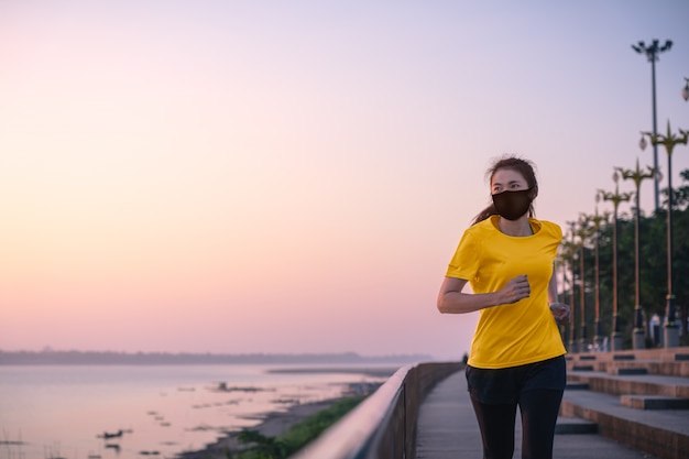 Asian woman running and exercise with wearing a protective mask
covid-19 an outdoor workout on the riverwalk in the morning.