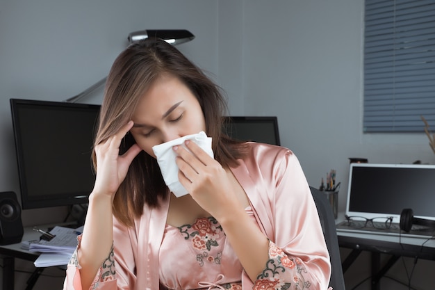 Asian woman in satin nightwear feeling unwell and sneeze on desk at home