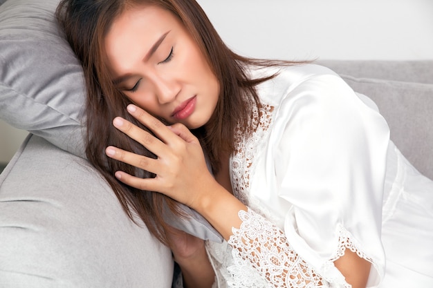 Asian woman in a satin sleepwear whiteredfaced because of fever and feverish Body Temperature