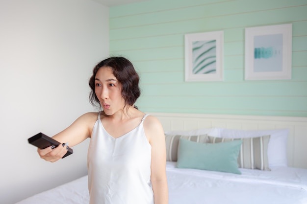 Asian woman shocked and feeling wow when turning on the tv with\
the remote control asian housewife checking social media with smart\
tv at home omg