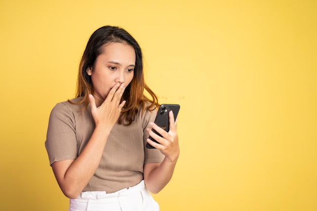 Asian woman shocked while looking at her mobile phone on isolated background