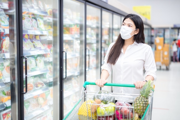 Asian woman shopping with mask safely buying for groceries , safety measures in supermarket.