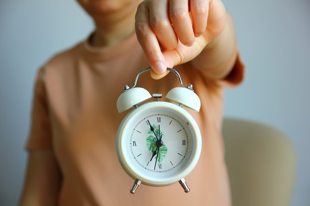 Asian woman showing alarm clock in hand