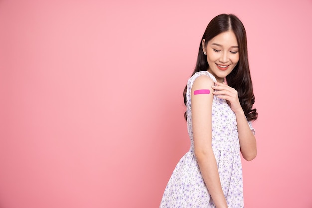 Photo asian woman showing arm with plaster of covid19 vaccinated isolated on pink studio background