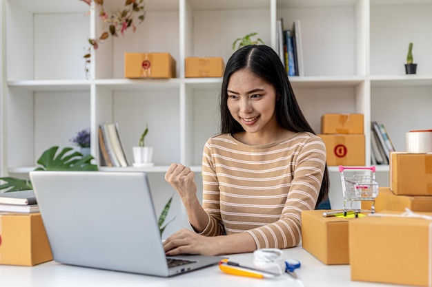 An Asian woman showing joy after reaching her daily sales target, she owns an online store, she packs and ships through a private transport company. Online selling and online shopping concepts.