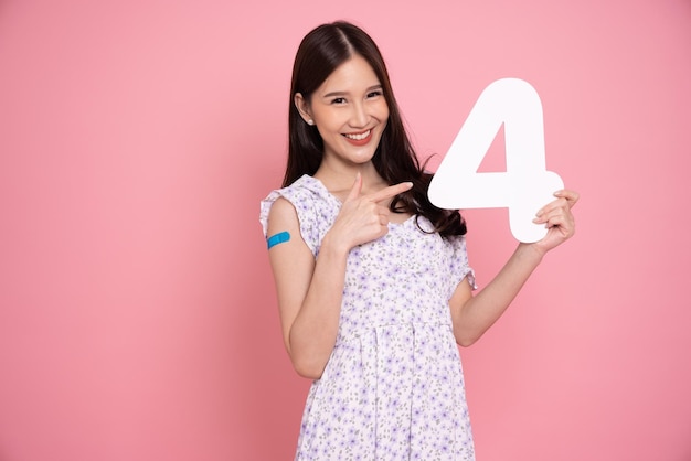 Asian woman showing number 4 with plaster of Covid19 Vaccinated isolated on pink studio background