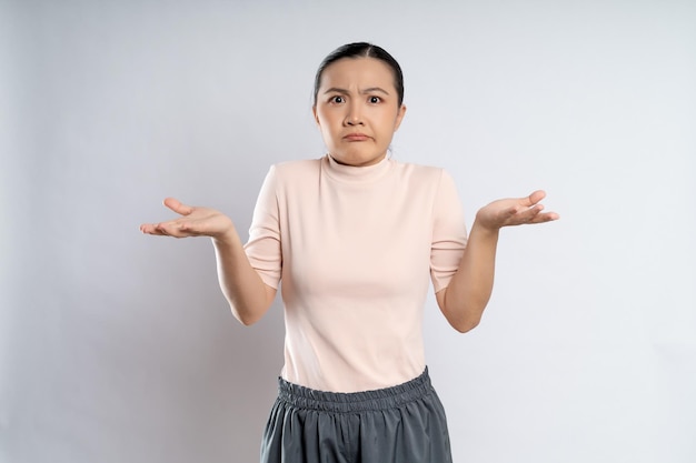 Asian woman shrugs her arms and makes gesturing of she don't know isolated over white background