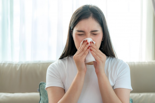 Asian woman sick and sad with sneezing on nose and cold cough on tissue paper because influenza and weak or virus bacteria from dust weather or smoke for medical.
