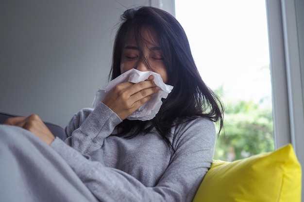 家のソファで病気のアジア人女性 インフルエンザによる高熱と鼻水で頭痛がする女性 インフルエンザによる病気の概念