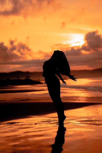Foto una donna asiatica in silhouette sta facendo un bellissimo ballo sulla spiaggia con le onde che si infrangono