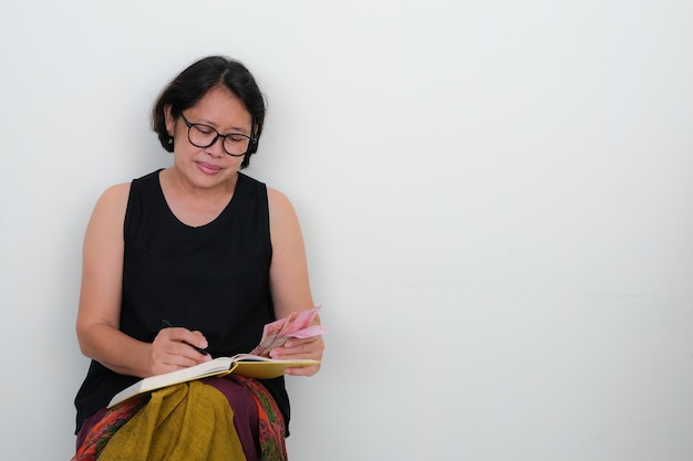 Asian woman sitting alone writing notes in her book on her lap