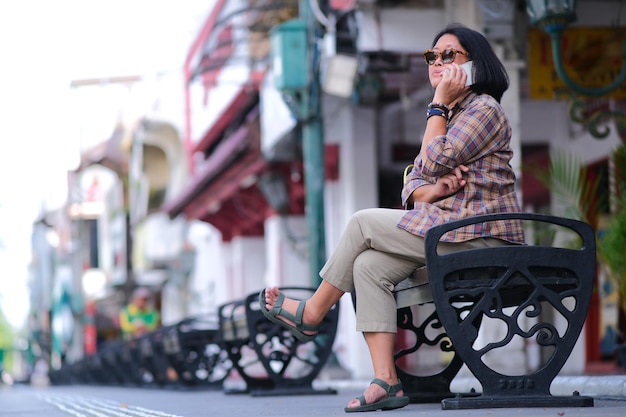 Asian woman sitting on a bench on iconic Malioboro street of Yogyakarta making a phone call