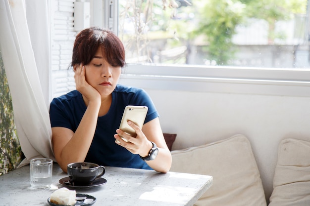 Азиатская женщина сидит в кафе и ждет уведомления на своем смартфоне
