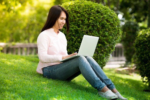 Asian woman sitting green park using laptop computer Woman working on laptop happy entrepreneur