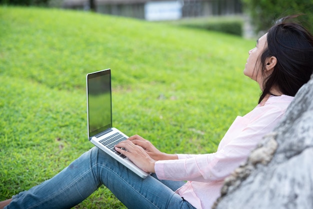 Asian woman sitting green park using laptop computer Woman working on laptop happy entrepreneur